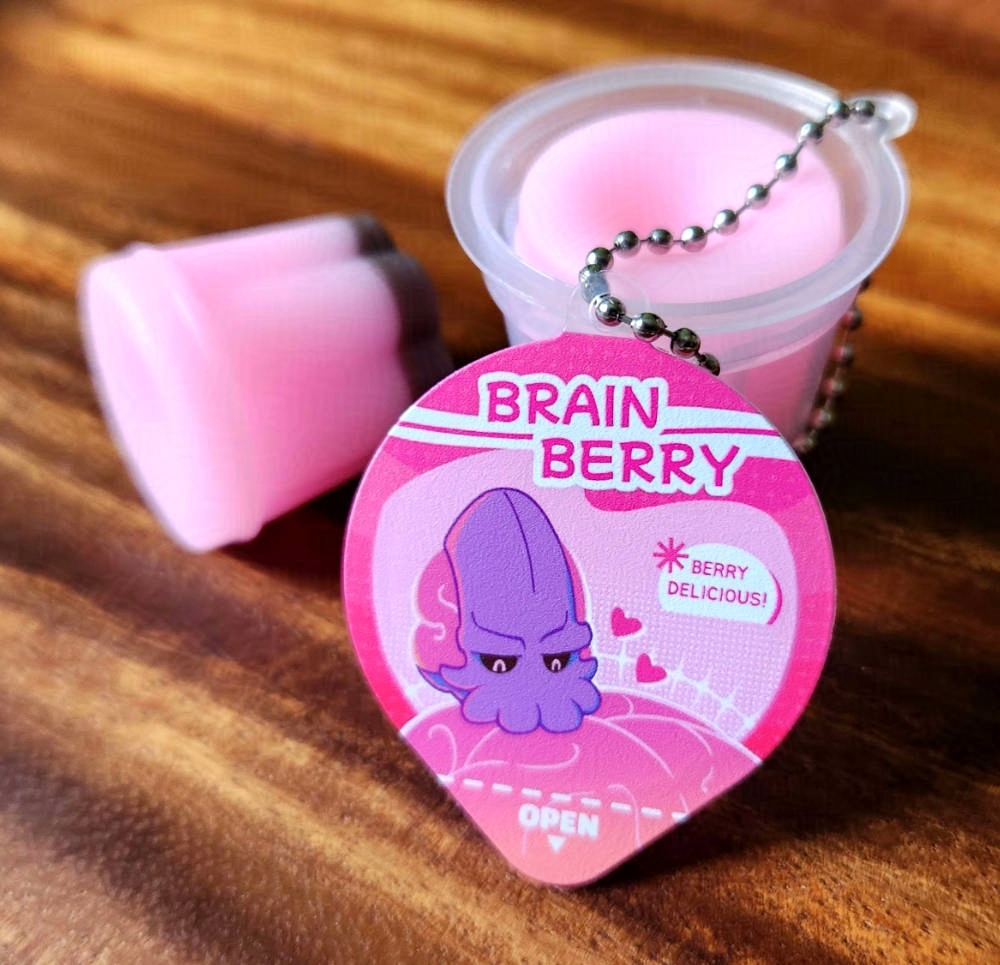 A little pink pudding cup with a little Emperor blorbo on the cover. He's nibbling on a brain. The name of the cup is Brain Berry (*berry delicious).